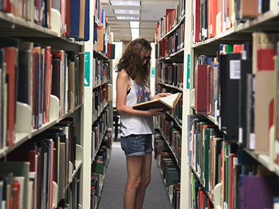 woman looking at a book in the stacks of a library