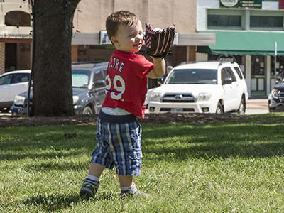boy catching a baseball with parked cars in the background