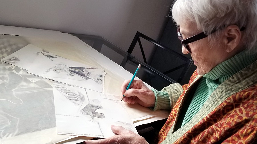 photograph of a woman sketching surrounded by drawings on a table
