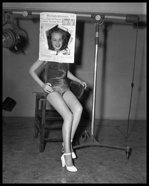 photograph of young woman in a bathing suit looking through a cutout
newspaper